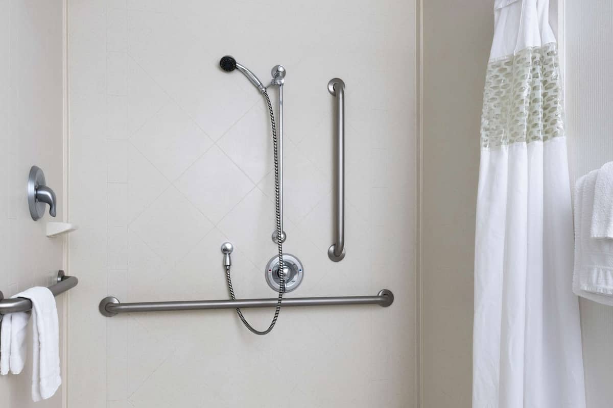 Ein modernes Badezimmer mit begehbarer Dusche, Haltegriffen und einem weißen Duschvorhang.