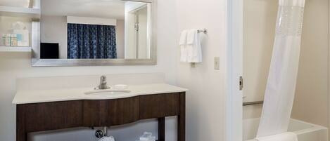 A bathroom with a sink, mirror, and shower area.
