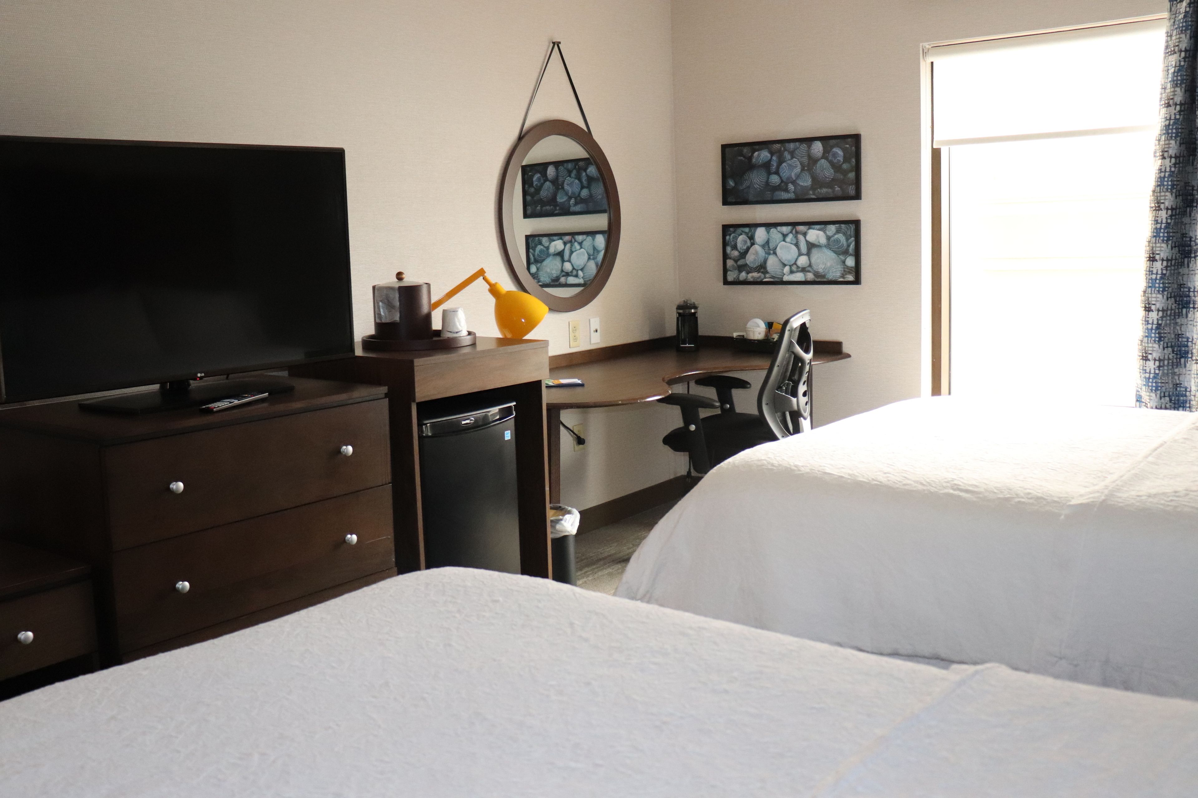 Een hotelkamer met een bed, een bureau met stoel, een televisie, een lamp en kunst aan de muur.