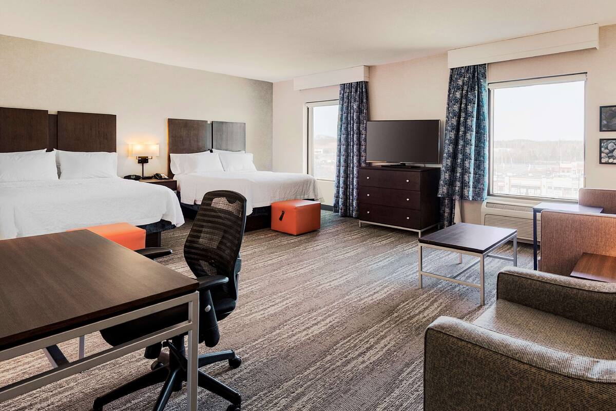 Ein Hotelzimmer mit zwei Betten, einem Schreibtisch, einem Stuhl, einem Fernseher und einem Sofa.