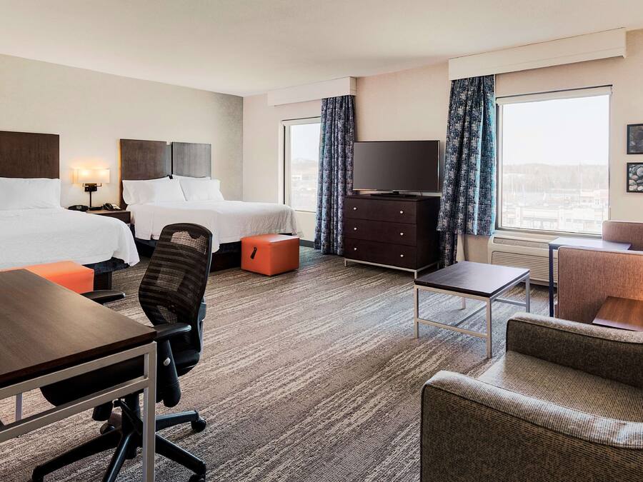 A hotel room with two beds, a desk, a chair, a TV, and a sofa.