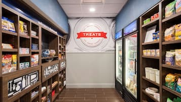 A corridor with shelves stocked with snacks and treats, a refrigerated display case, and a wall with a 'Treats' sign.