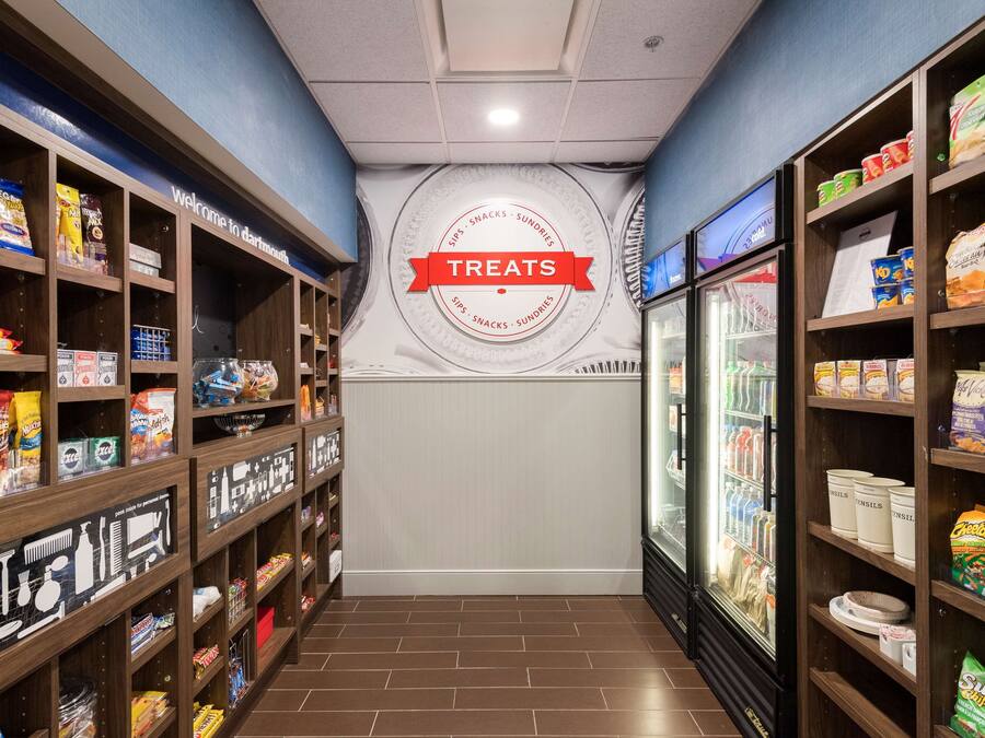 A corridor with shelves stocked with snacks and treats, a refrigerated display case, and a wall with a 'Treats' sign.