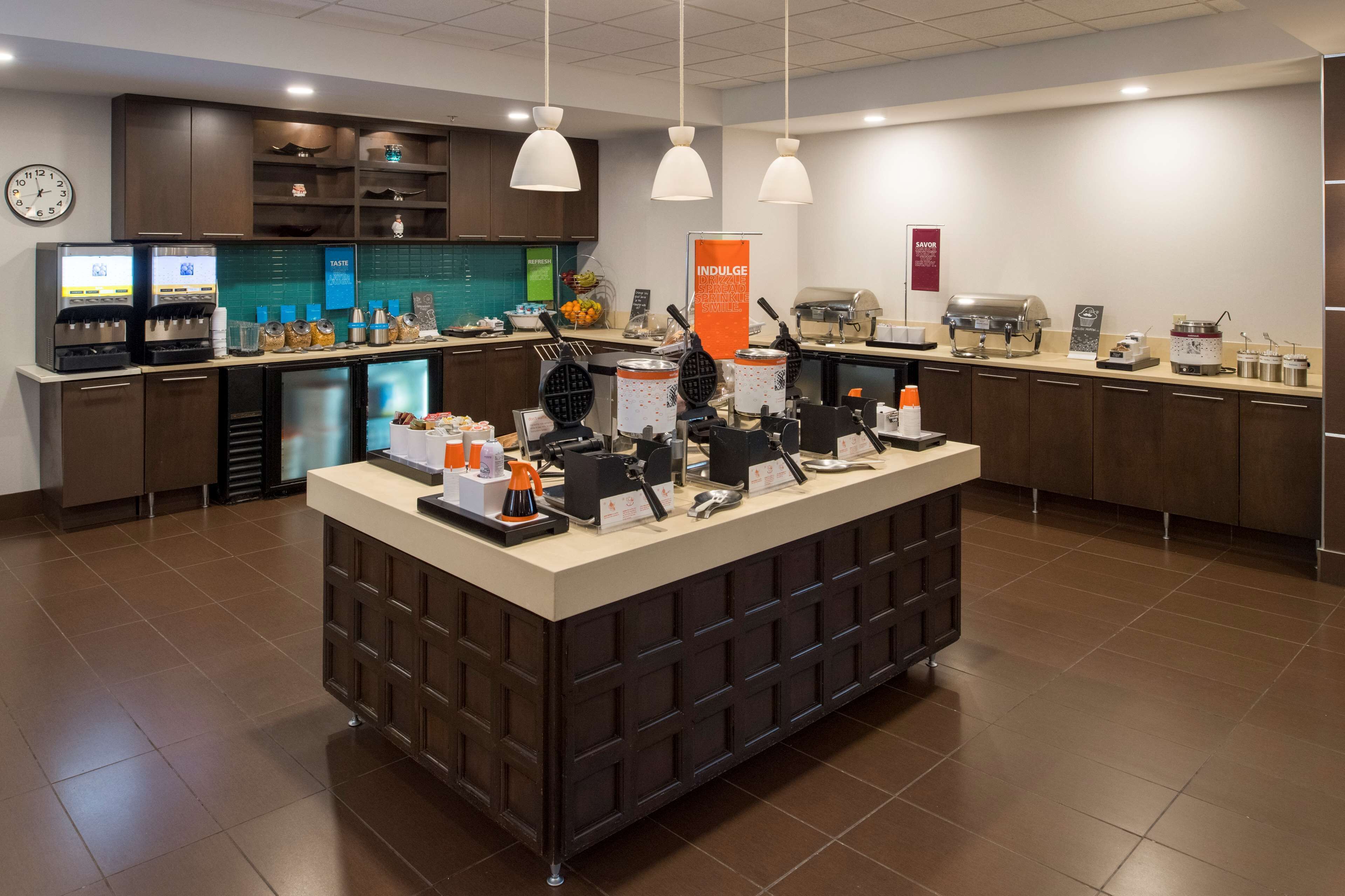 A self-service breakfast area with waffle makers, coffee machines, and a variety of food items.
