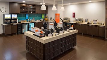 A self-service breakfast area with waffle makers, coffee machines, and a variety of food items.