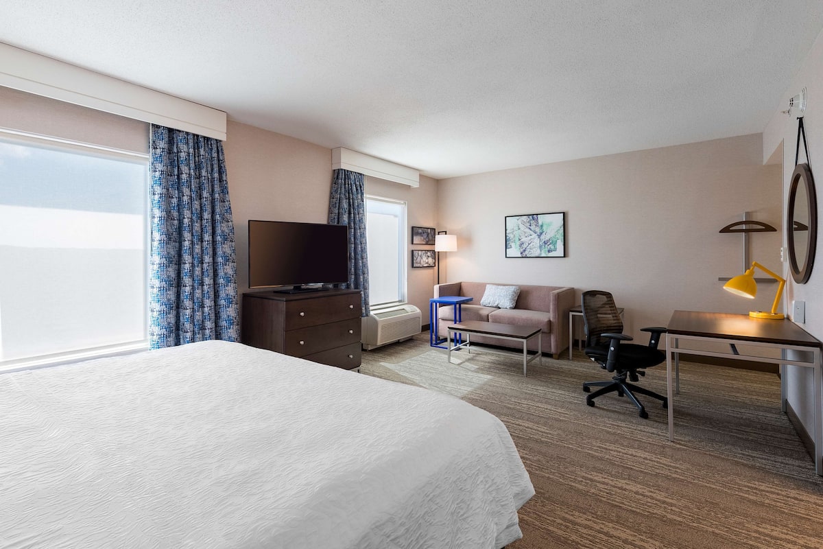 Ein Hotelzimmer mit einem großen Bett, einem Schreibtisch mit Stuhl, einem Fernseher und einer Schreibtischlampe.