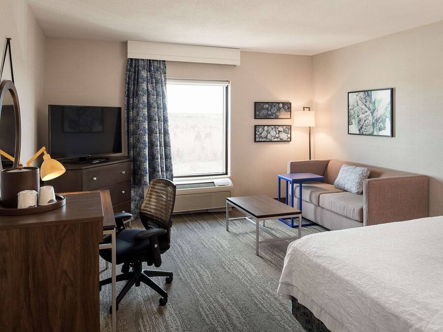 Una habitación de hotel con una cama, un escritorio con silla, televisor, lámpara y sofá.