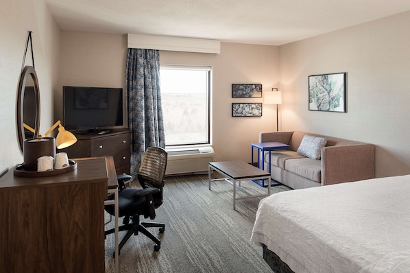 A hotel room with a bed, a desk with a chair, a television, a lamp, and a couch. - Hampton Inn & Suites by Hilton Halifax - Dartmouth (Dartmouth)