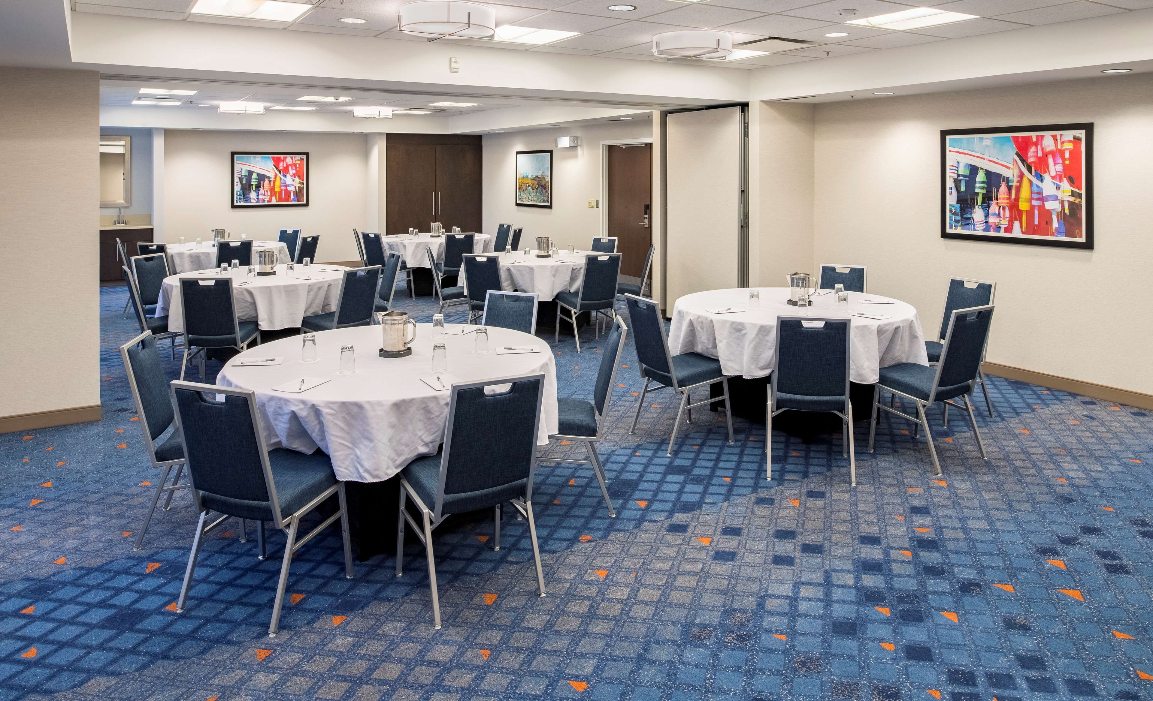 A conference room with round tables, chairs, and white tablecloths.