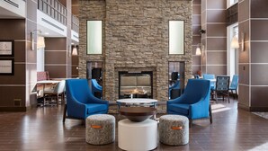 A lobby with a stone fireplace, blue chairs, and a round table. - Hampton Inn & Suites by Hilton Halifax - Dartmouth (Dartmouth)