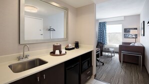 A modern hotel room with a large mirror, a sink, a coffee maker, and a seating area with a sofa and a small table. - Hampton Inn & Suites by Hilton Halifax - Dartmouth (Dartmouth)