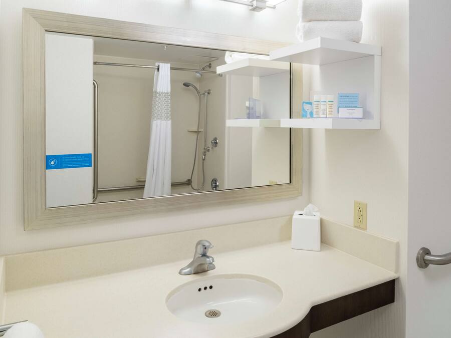 Un baño con lavamanos, espejo, ducha y toallero.