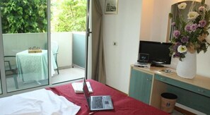Un dormitorio con una cama, una computadora portátil, un televisor y un florero con flores.
