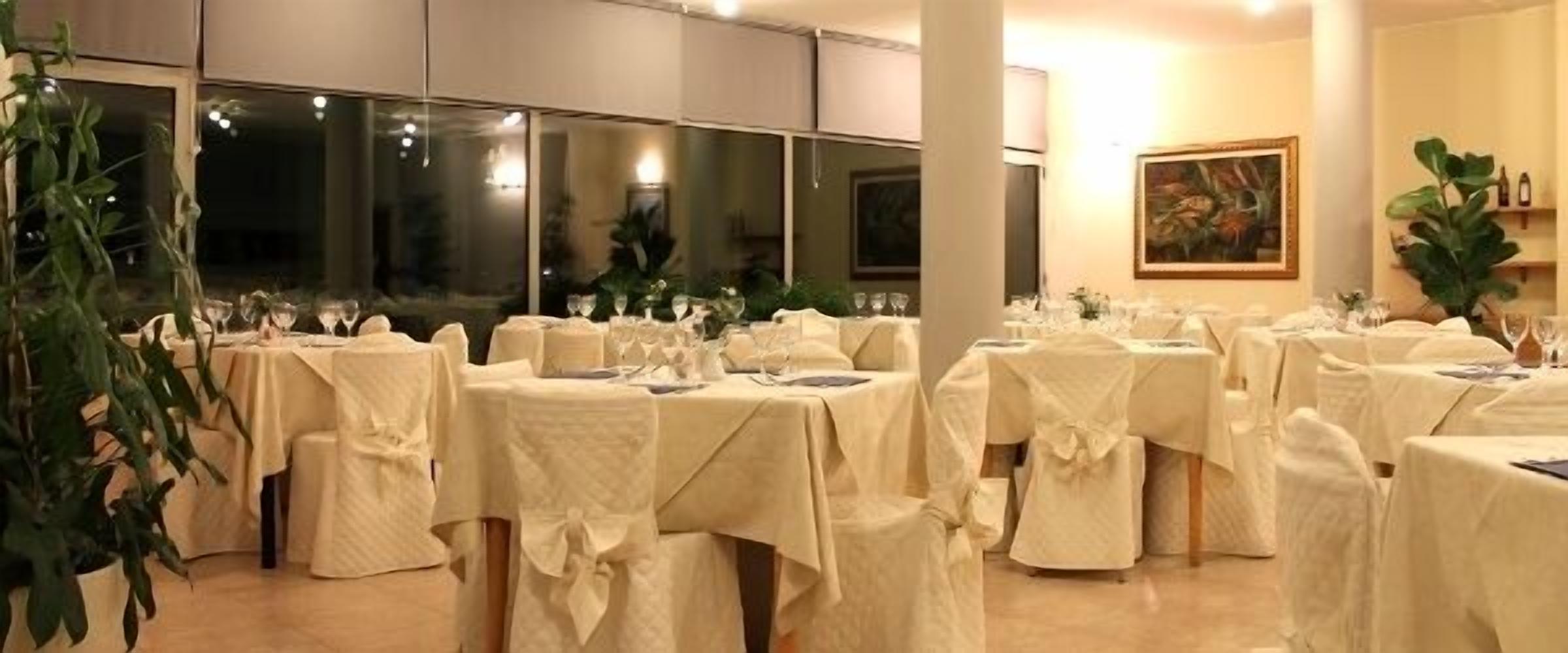 Un salón de banquetes con mesas redondas cubiertas con manteles blancos, sillas con fundas blancas y un amplio ventanal al fondo.