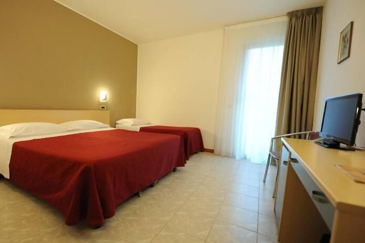 A hotel room with two beds, a desk with a computer, and a window with curtains.