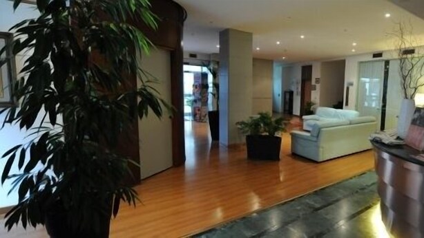 A spacious living area with a wooden floor, a light-colored sofa, a small table, and a potted plant. - Hotel Elvezia (Pesaro)