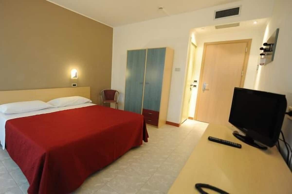 A hotel room with a bed, a TV, a desk, and a wardrobe.