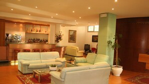 A spacious living area with a sofa set, a coffee machine, and a bar area with shelves of bottles. - Hotel Elvezia (Pesaro)