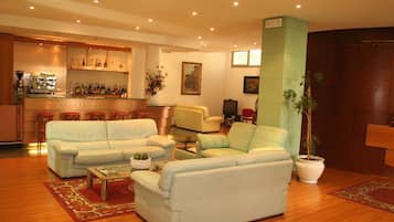 Amplia sala de estar con un conjunto de sofás, una máquina de café y una zona de bar con estantes llenos de botellas.