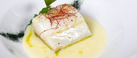 A white plate with a piece of white fish, garnished with red strands and a green leaf, served on a white plate.