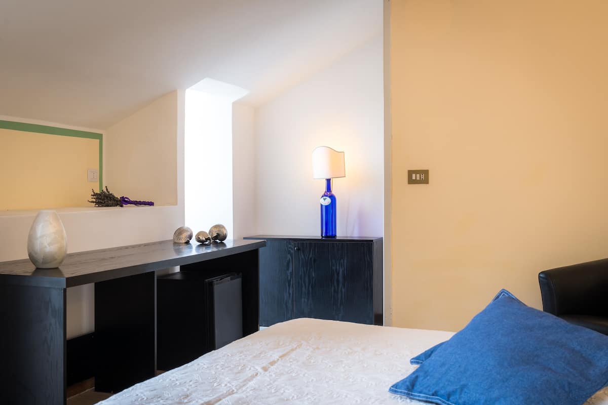 Ein Schlafzimmer mit Bett, Schreibtisch, Lampe und Fenster.