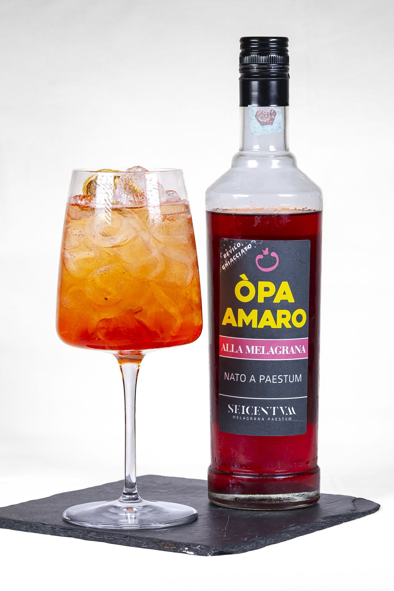 Una botella de BeVilo BeVincio Opa Amaro con etiqueta y un vaso de la bebida con hielo.