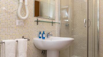 A bathroom with a white sink, two blue bottles, a glass shelf, and a glass shower enclosure.