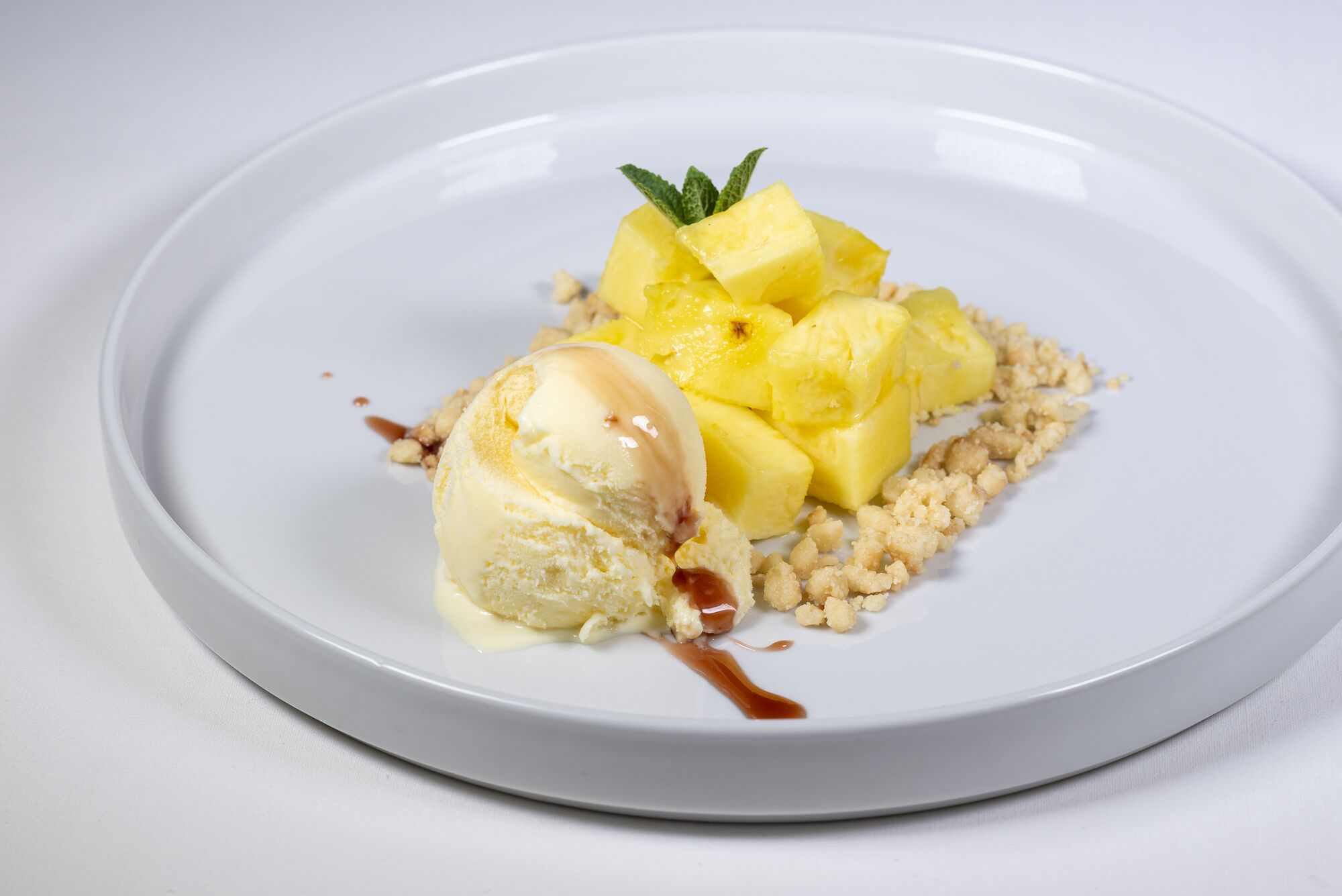 A dessert plate with a scoop of vanilla ice cream, diced pineapple, and crumbled biscuit.