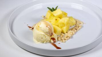 Ein Dessertteller mit einer Kugel Vanilleeis, Ananaswürfeln und zerbröseltem Keks.