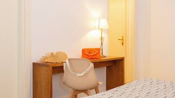 A room with a wooden desk, a chair, a lamp, a bed, and a door.