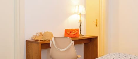 Una habitación con un escritorio de madera, una silla, una lámpara, una cama y una puerta.