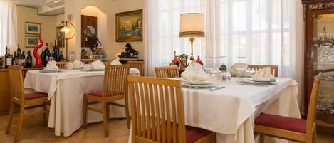 A dining area with multiple tables set for service, wooden chairs, and a large window with curtains.