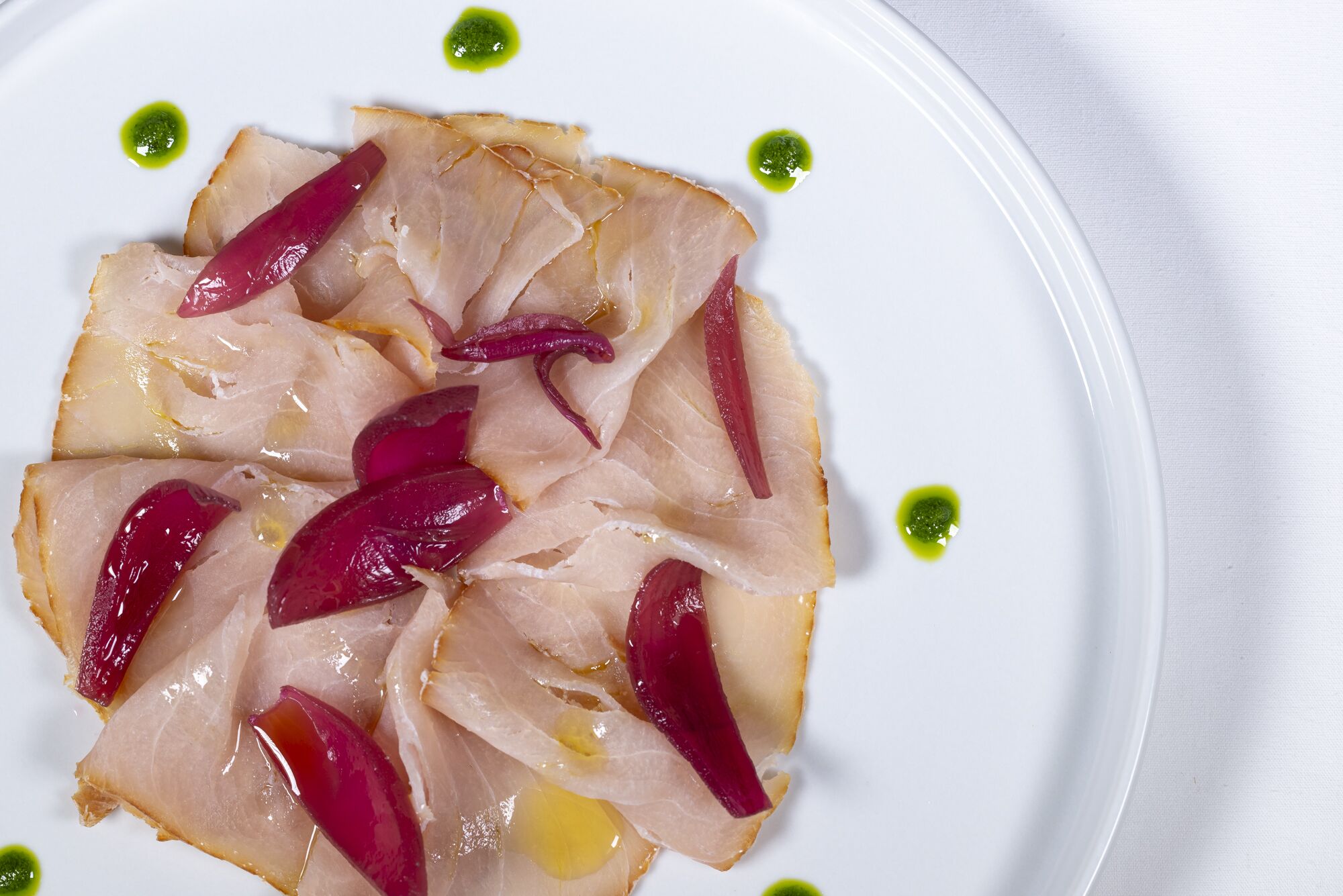 Ein Teller mit Essen, dünn geschnittenem Fleisch und roten Zwiebelringen, verziert mit grüner Soße.
