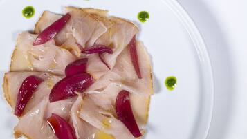 Ein Teller mit Essen, dünn geschnittenem Fleisch und roten Zwiebelringen, verziert mit grüner Soße.