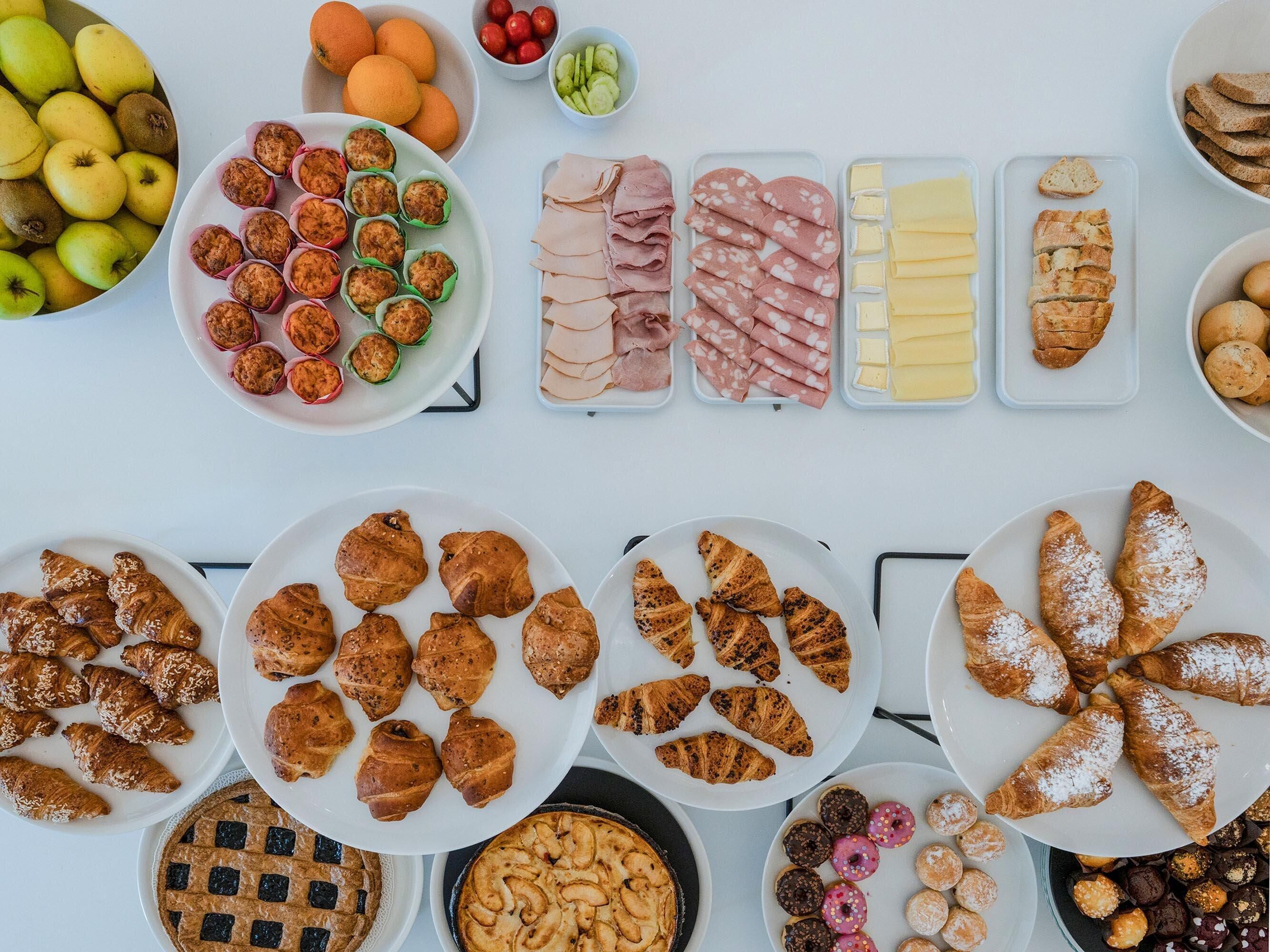 Diversos alimentos, incluindo frutas, doces e fatias de charcutaria, dispostos sobre uma mesa.