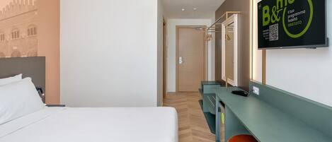 Una habitación de hotel con una cama, un escritorio con una silla, un espejo y un cartel en la pared.