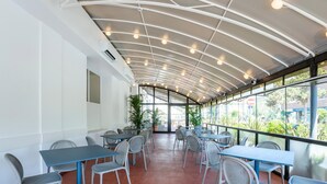 A covered outdoor seating area with tables and chairs, large windows, and a curved ceiling structure. - B&B HOTEL Pesaro Des Bains (Pesaro)