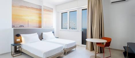 A hotel room with two beds, a small table, a chair, and a view of a Ferris wheel through a window.