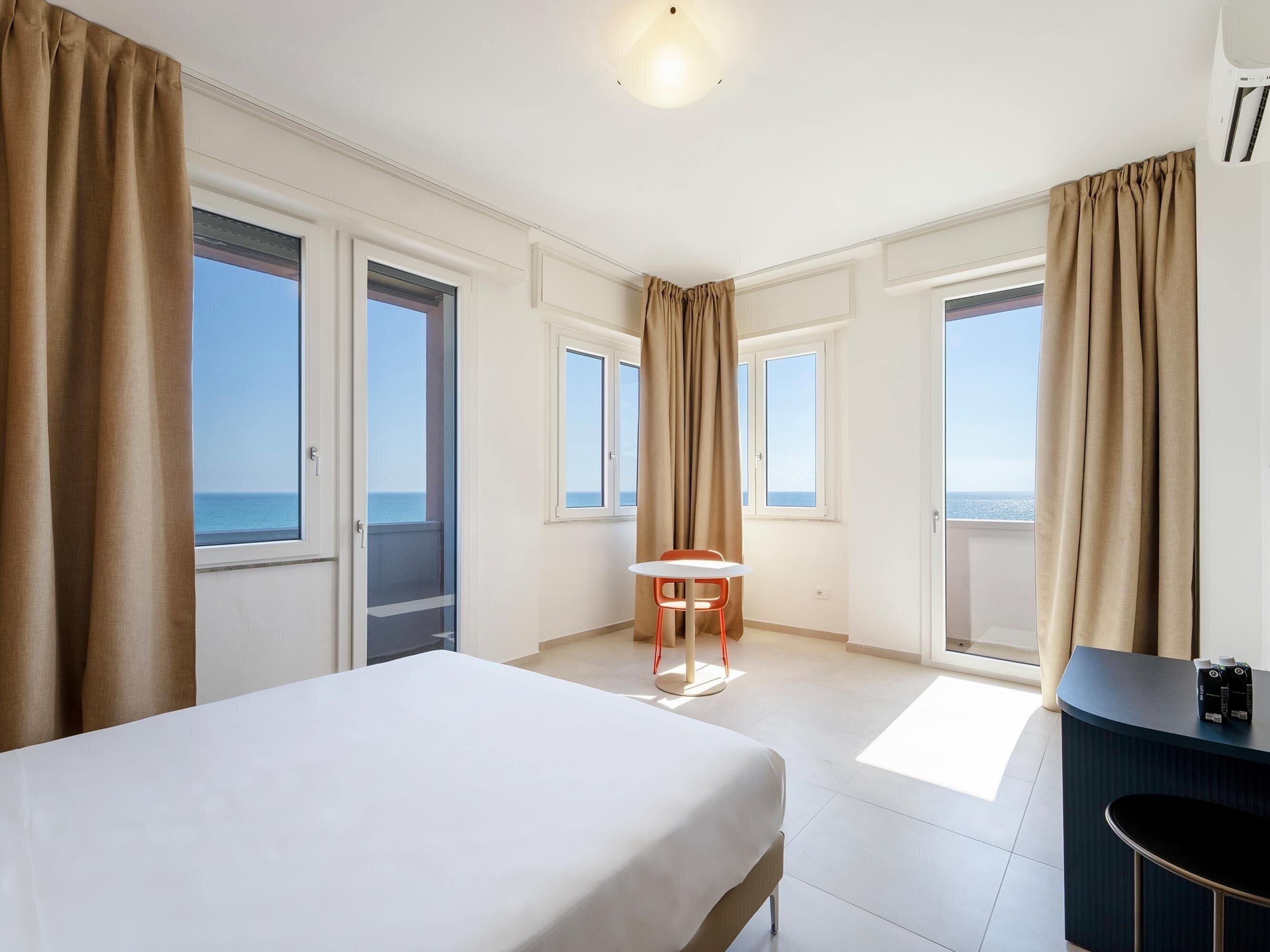 Una camera d'albergo con un letto, un tavolino, una sedia e un mini-frigo.