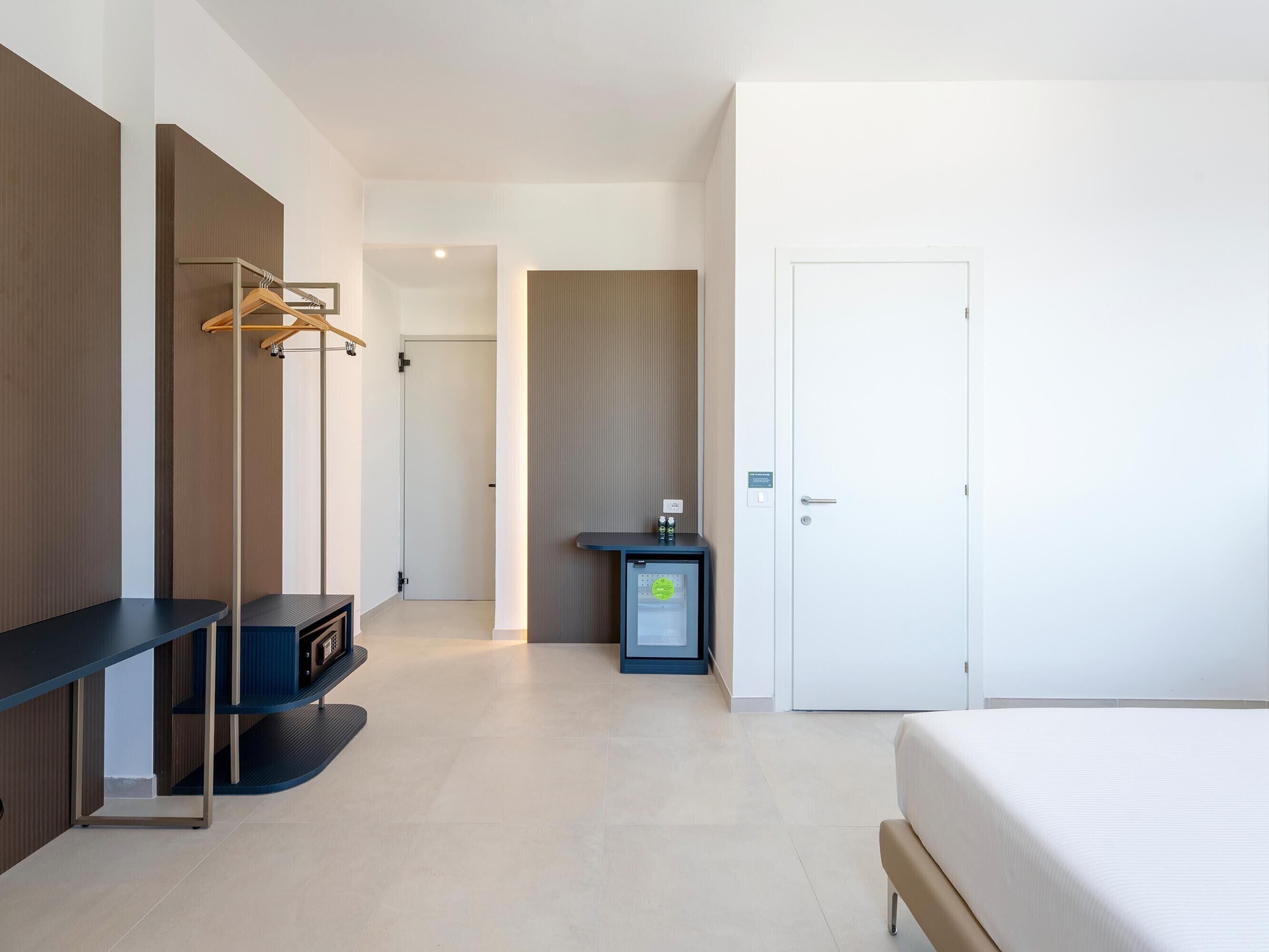 Una habitación de hotel moderna con cama, escritorio, perchero y minibar.