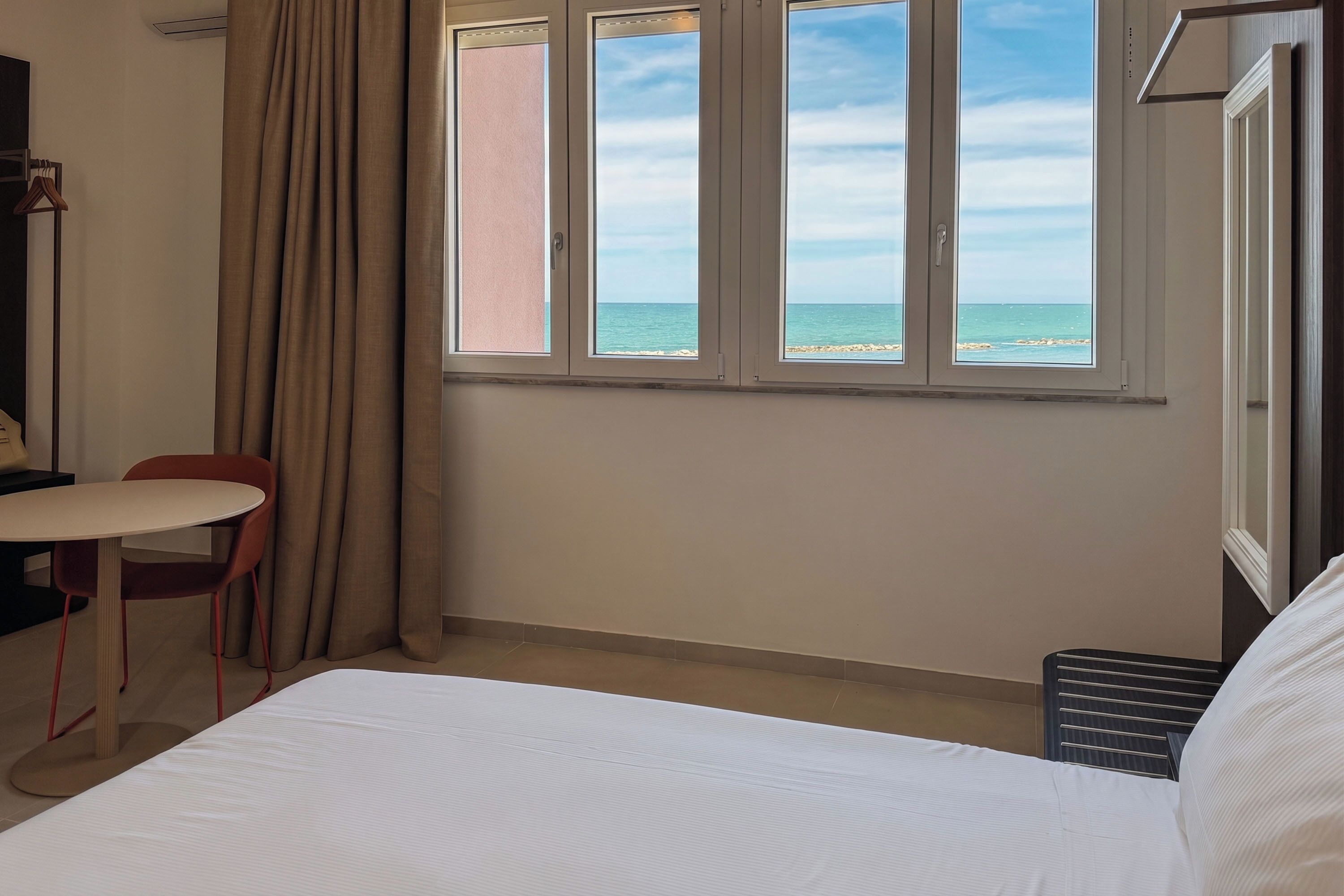 Ett hotellrum med en säng, ett bord, en stol och ett fönster med utsikt över stranden.