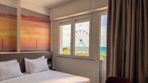 Una habitación de hotel con una cama, un ventanal con vista a una noria y una mesa.