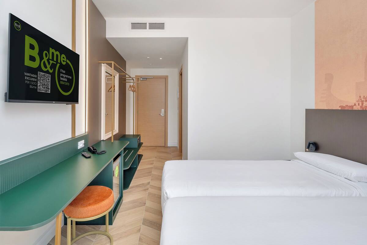 Une chambre d’hôtel comprenant un lit, un bureau avec une chaise, un porte-manteau et un téléviseur fixé au mur qui affiche un message.