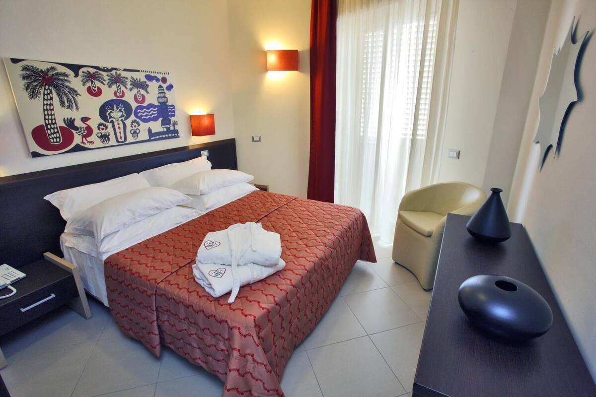 A hotel room with a bed, a nightstand, a desk, a chair, and a painting on the wall.