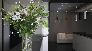 A modern kitchen with a white countertop, a vase with flowers, and a white sofa in the background. - Noha Suite Hotel (Riccione)