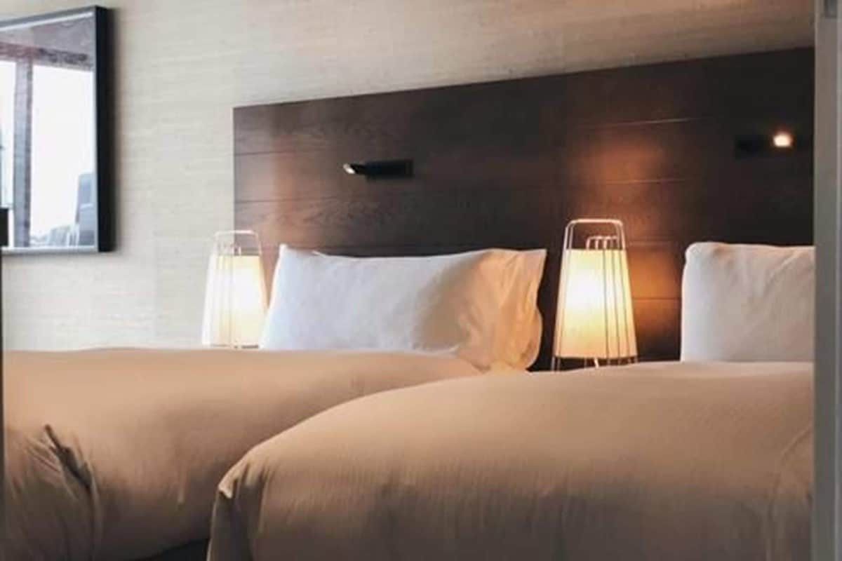 A hotel room with two beds, a wooden headboard, bedside lamps, and a framed picture on the wall.