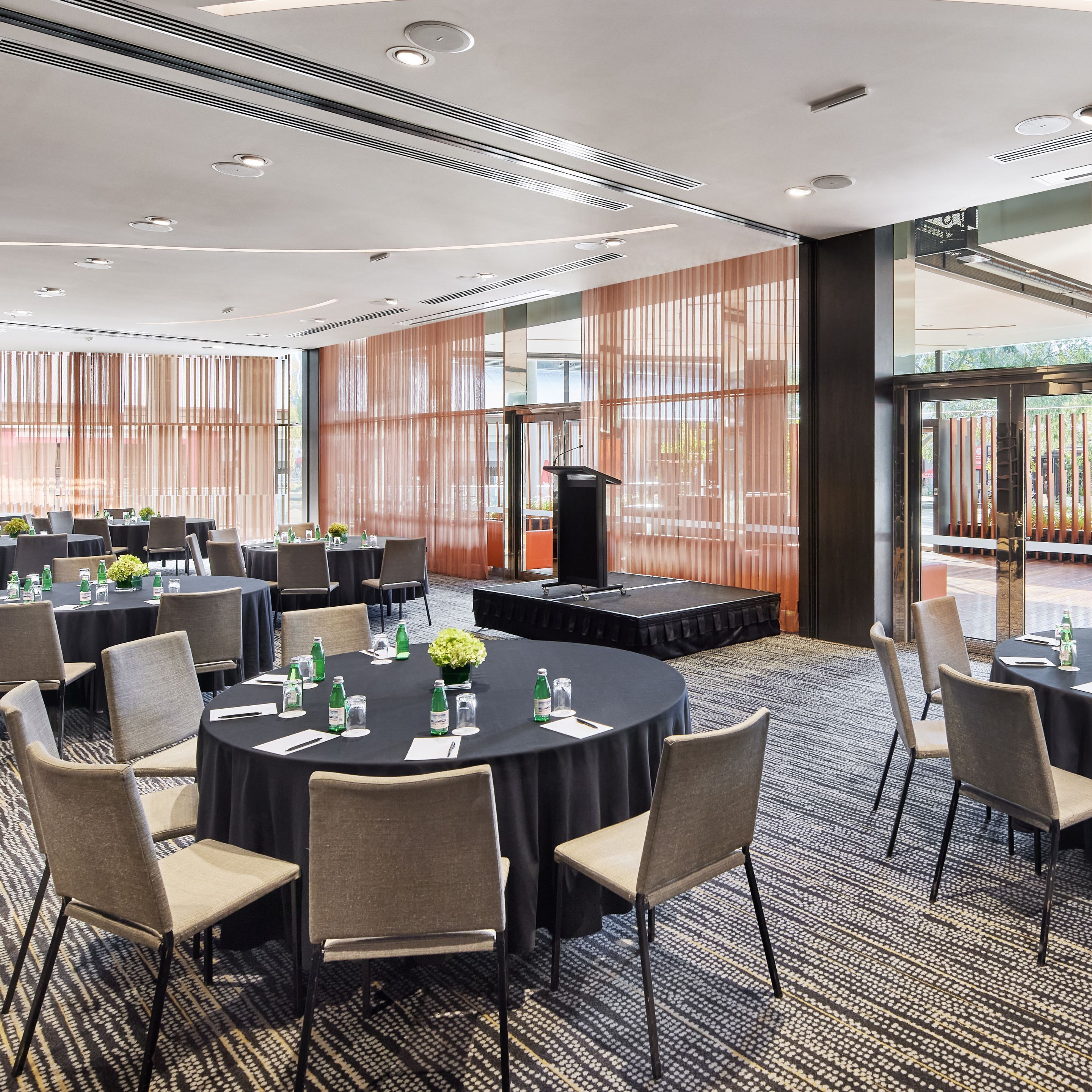 A conference room with round tables, chairs, and a stage with a podium.