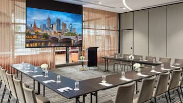 A conference room with a large screen displaying a cityscape, a long table with chairs, and a carpeted floor.