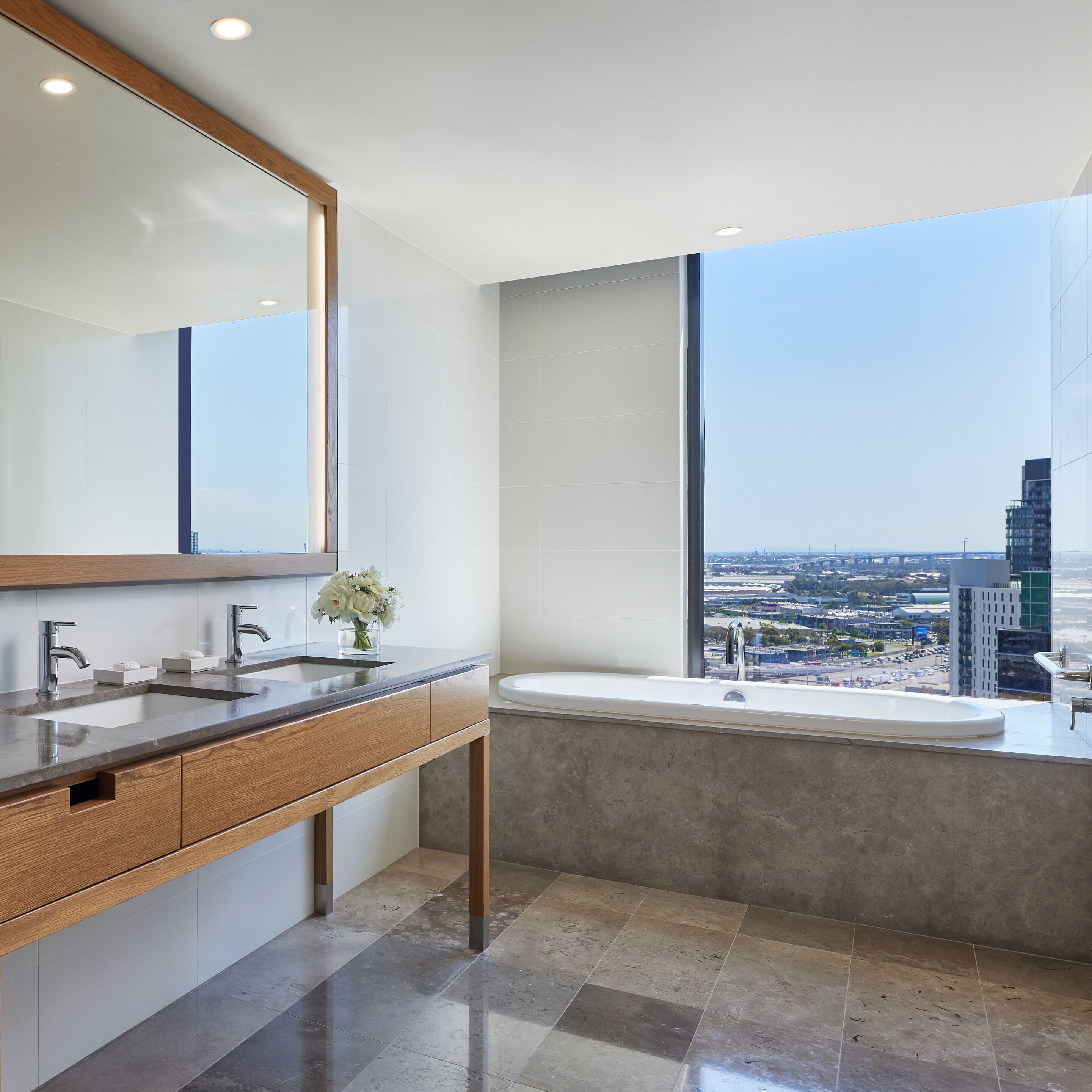 Un baño moderno con un espejo grande, lavamanos dobles y una bañera.