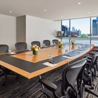 A conference room with a long table, chairs, and a city view through large windows.